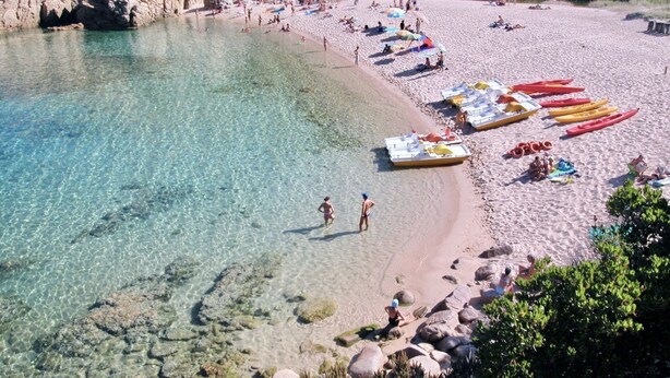 Ein Strand mit klarem Wasser, felsigem Gelände und am Ufer aufgereihten Kanus.