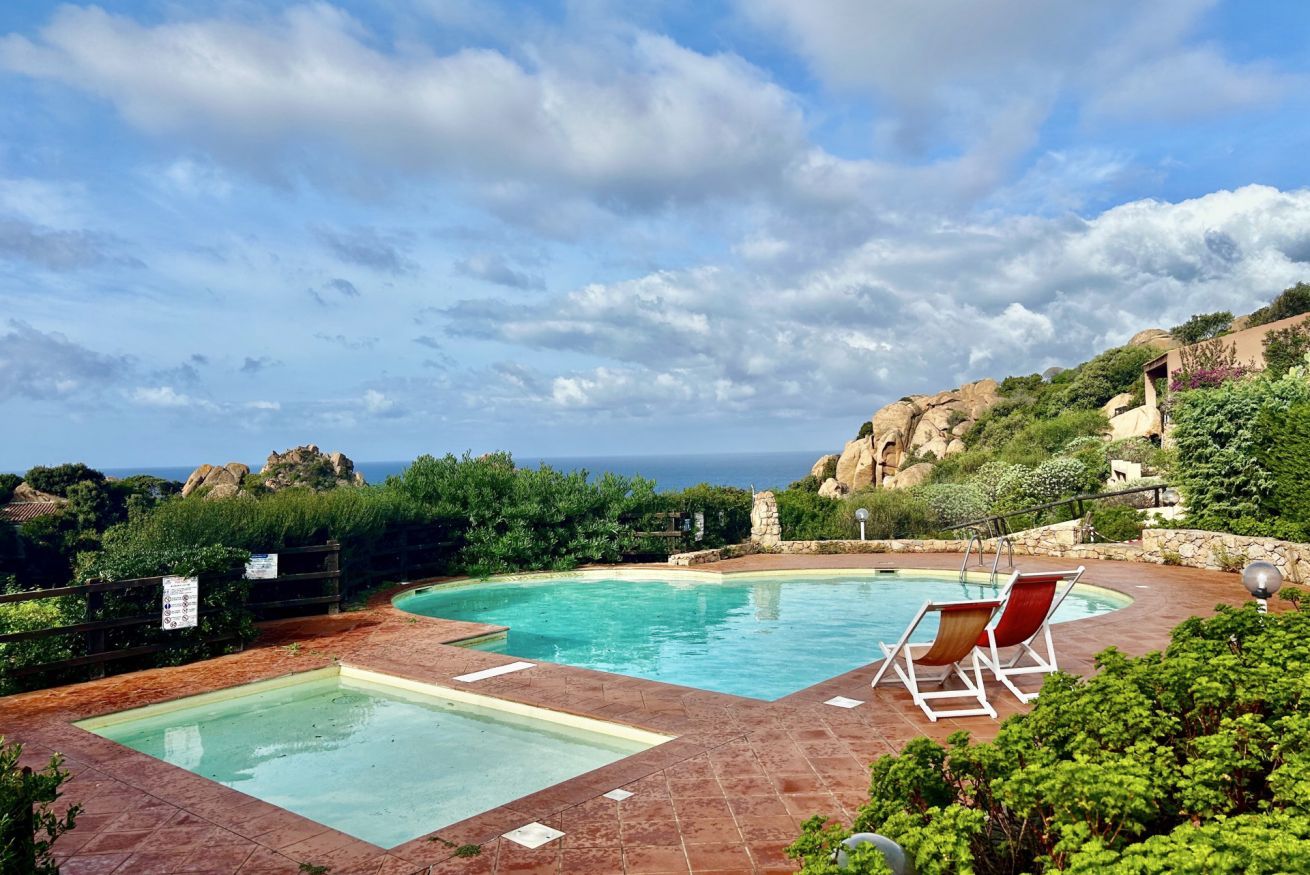 Ein Poolbereich mit zwei separaten Pools, umgeben von viel Grün und Blick auf das Meer.