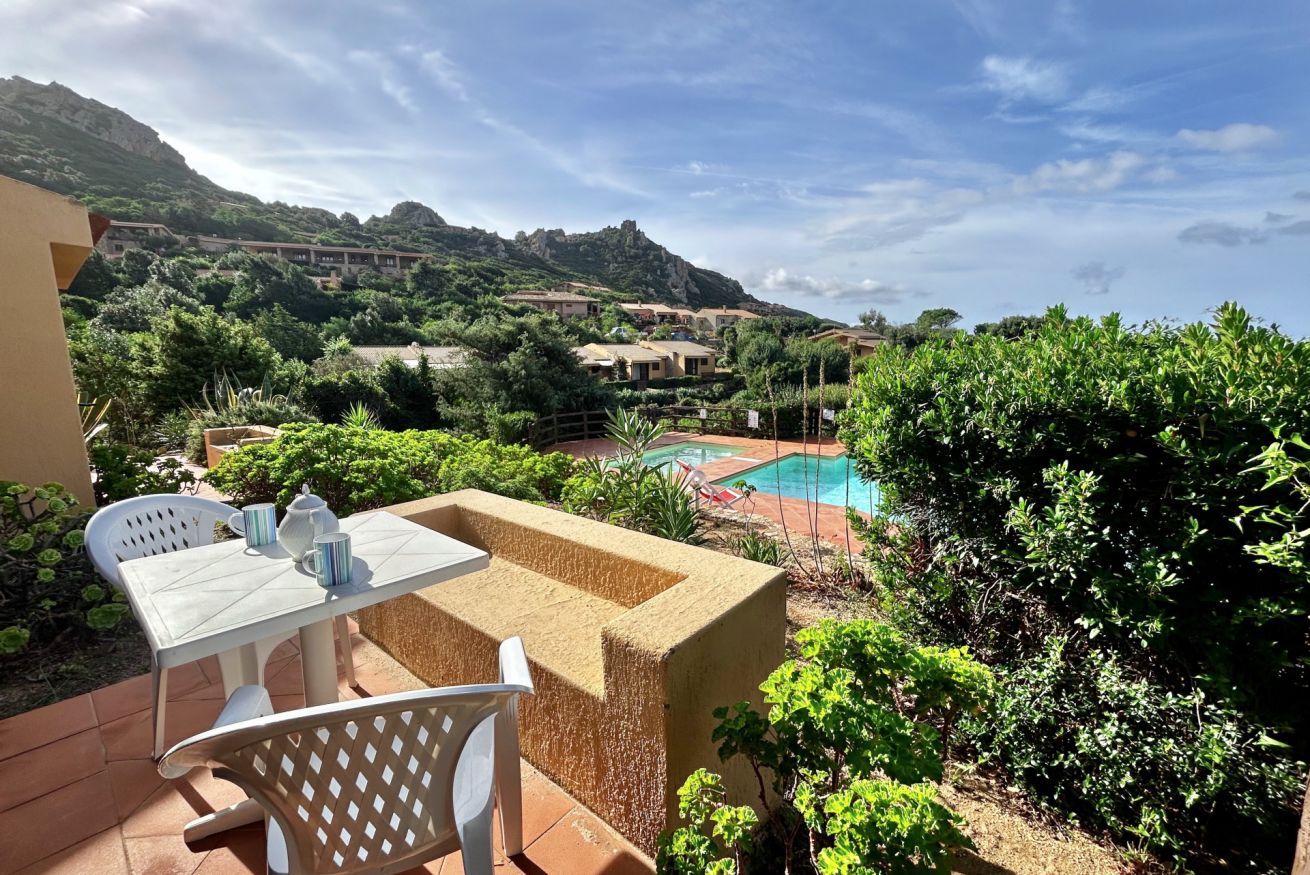 Eine Terrasse mit Tisch und Stühlen, ein Schwimmbecken und eine Bergkulisse im Hintergrund.