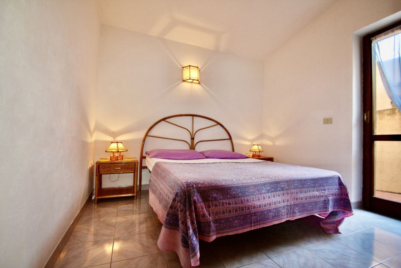 A bedroom with a bed, two bedside tables with lamps, a window, and a wall-mounted light fixture.