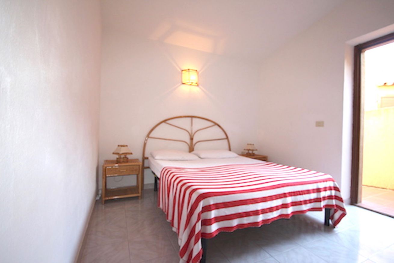 Een slaapkamer met een bed, nachtkastjes, een wandlamp en uitzicht door een geopende deur.