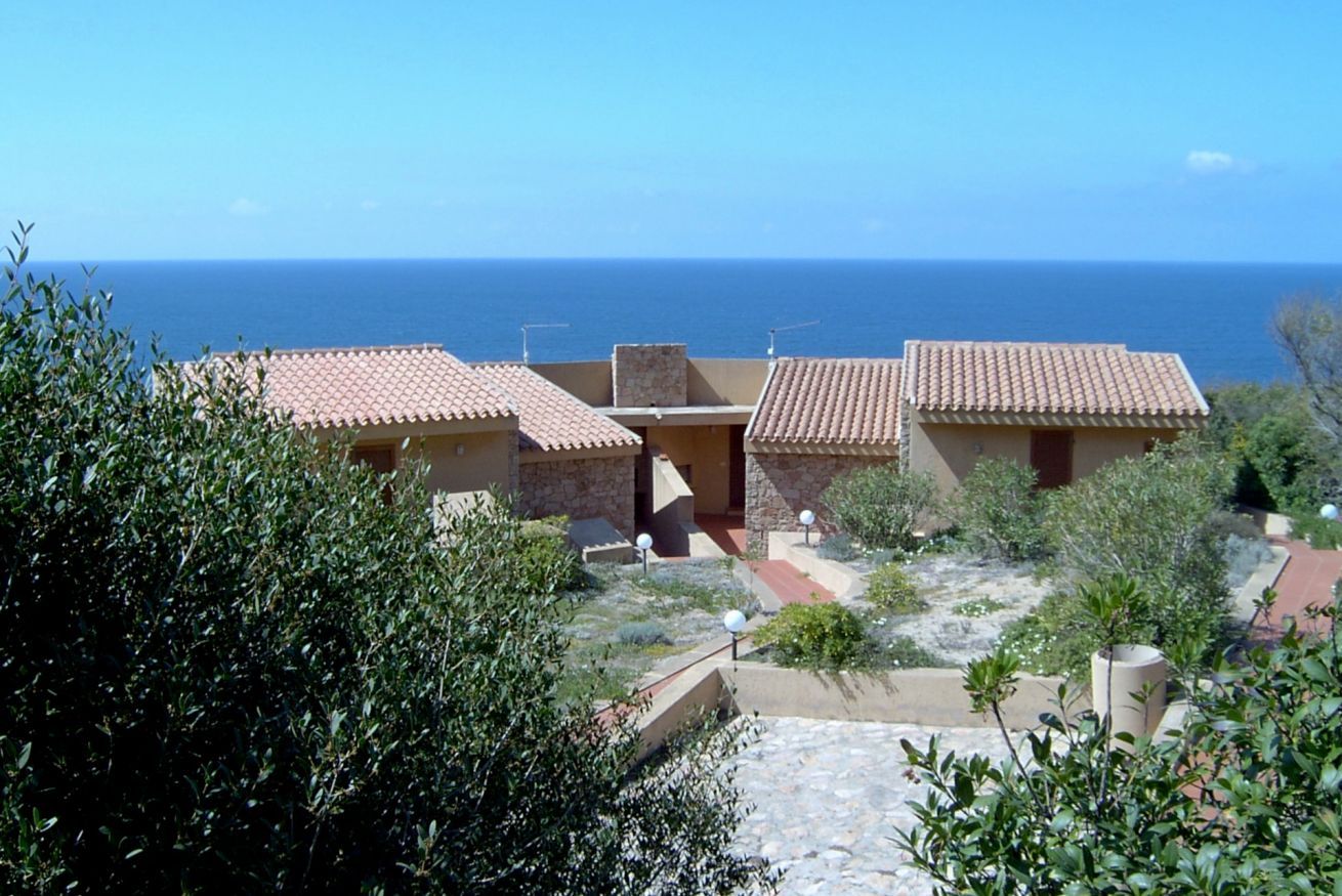 A coastal property with terracotta-roofed buildings, a stone pathway, and a view of the sea.