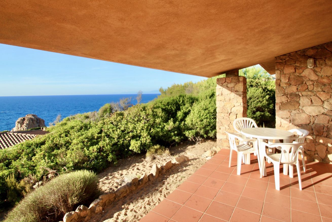 Eine Terrasse mit weißen Stühlen und einem Tisch, mit Blick auf eine Küstenlandschaft mit Meer und viel Grün.
