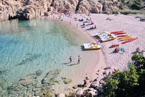 A beach with clear water, rocky terrain, and canoes lined up on the sand.