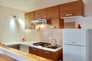 A kitchen with wooden cabinets, a gas stove, a sink, and a white refrigerator. - Two-room villa with sea view of approximately 40 m2 furnished in a simple and essential way comprising a living room with double sofa bed, kitchenette equipped with gas stove, a double bedroom with wardrobe and bathroom with shower.Covered veranda with o (Trinita' d'Agultu e Vignola)