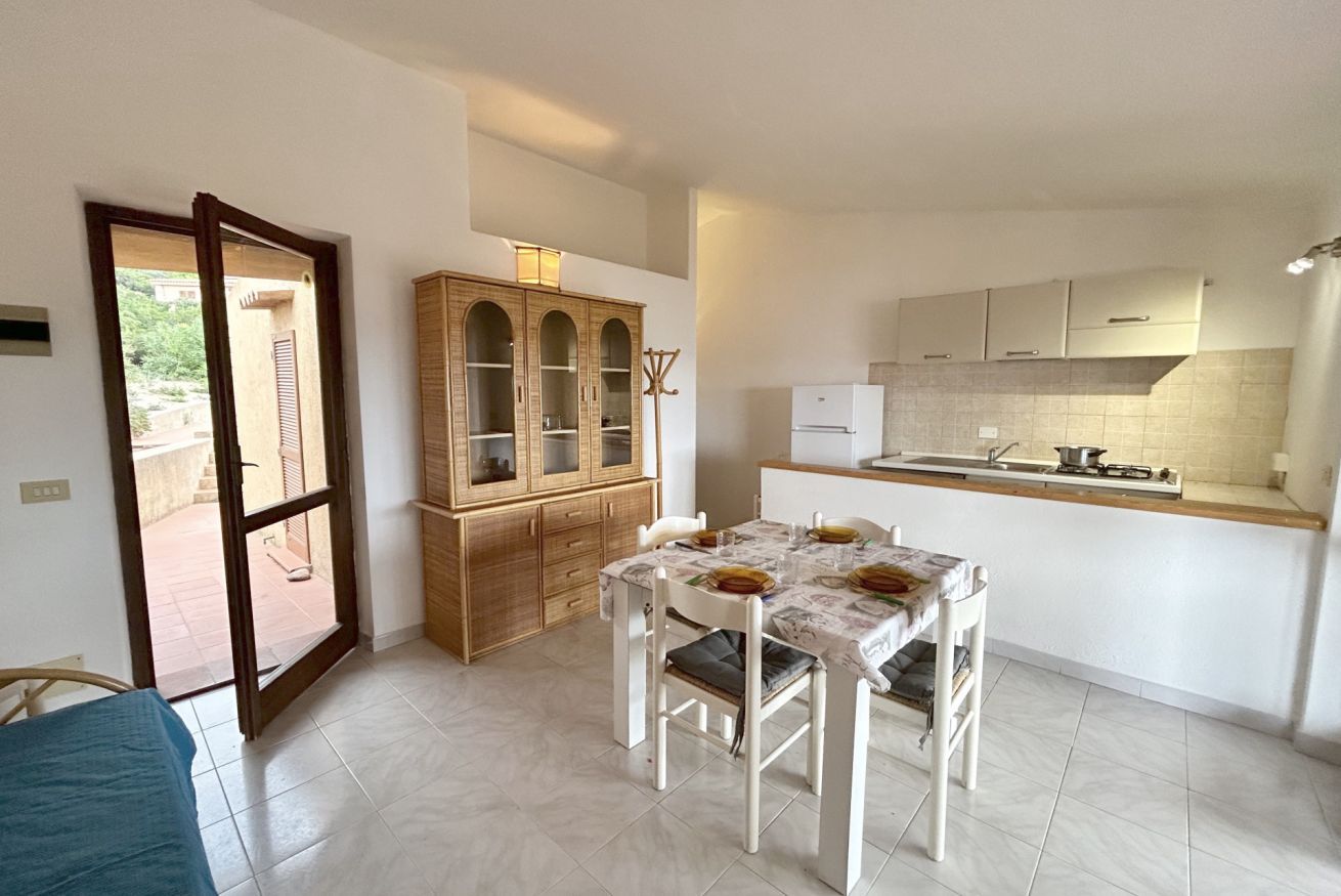 Una cocina compacta con una mesa de comedor lista para cuatro personas, un armario de madera y un ventanal corredero que da a un espacio exterior.