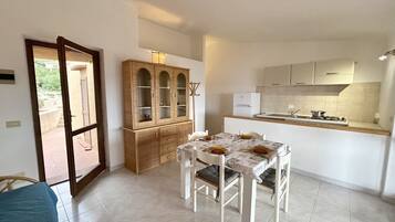 Una cocina compacta con una mesa de comedor lista para cuatro personas, un armario de madera y un ventanal corredero que da a un espacio exterior.