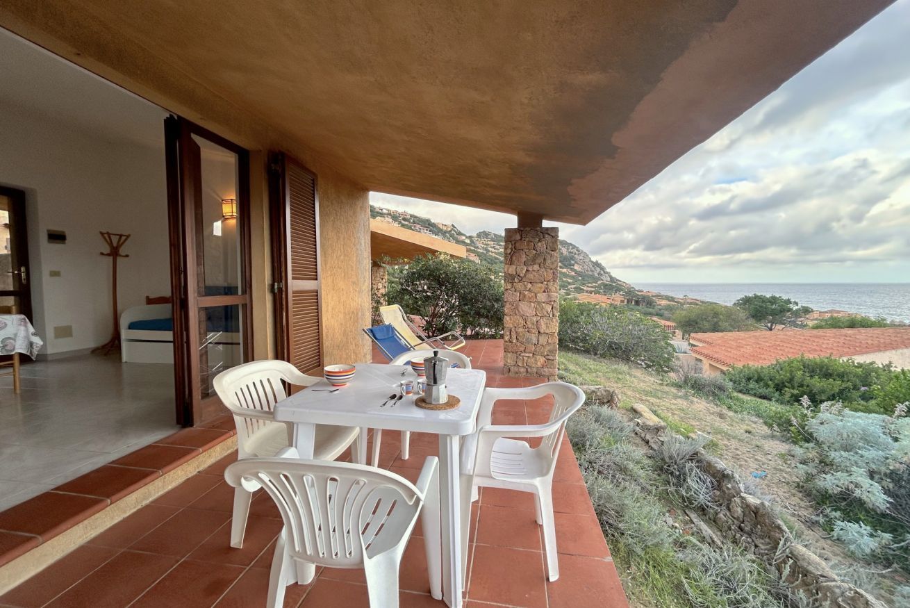 A patio with a table and chairs, a stone pillar, and a view of the sea and hills.