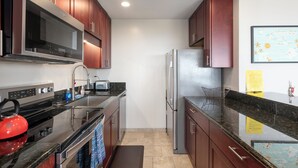 A compact kitchen with stainless steel appliances, wooden cabinets, and a granite countertop. - 🌴Beautiful condo located at higher elevations, Expansive Ocean Views🌴 (Holualoa)