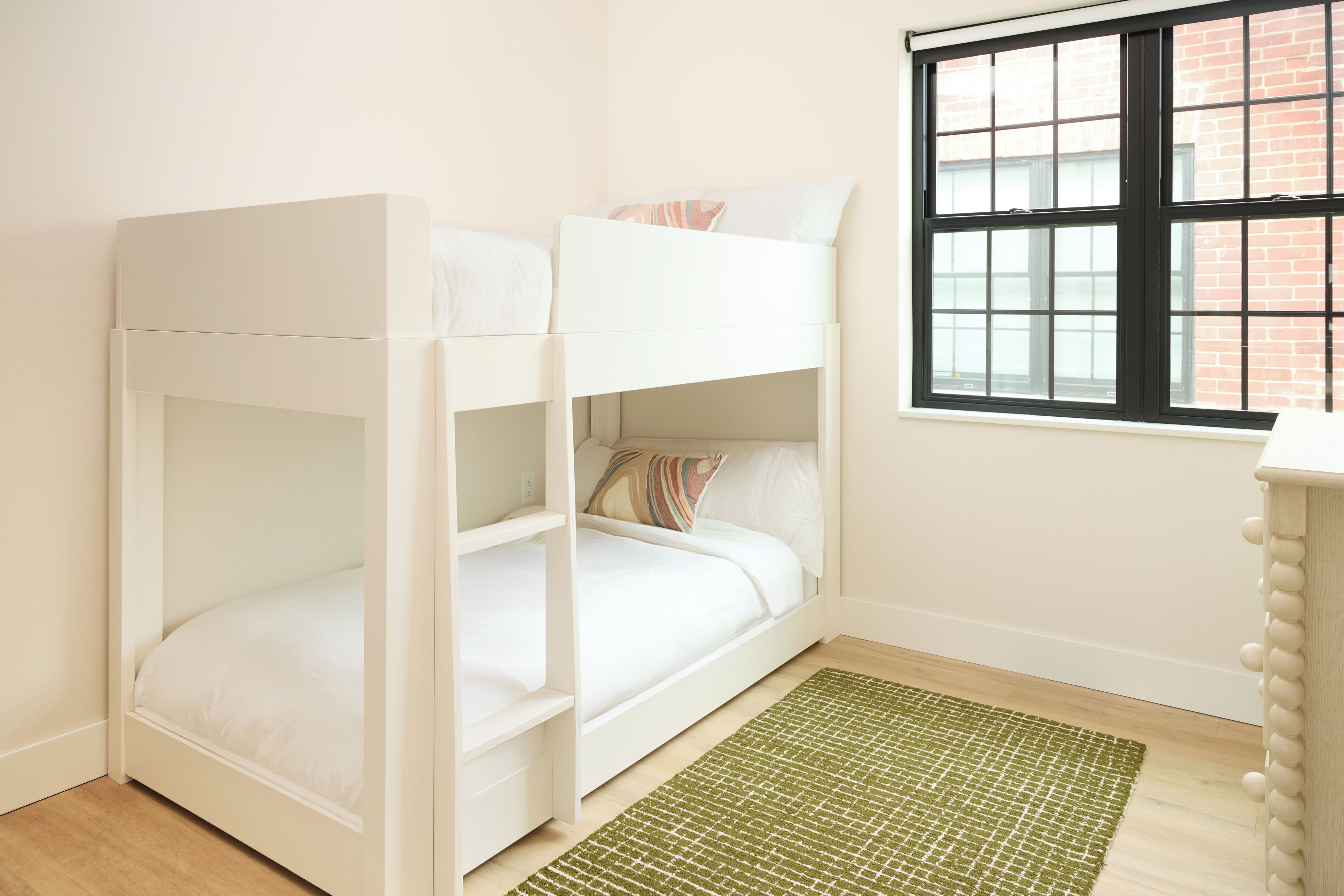 A bunk bed in a room with a window, a green rug, and a wooden dresser.