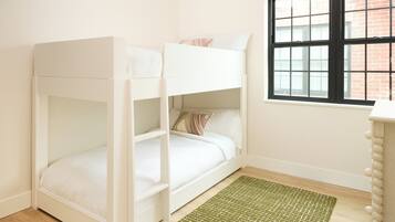 A bunk bed in a room with a window, a green rug, and a wooden dresser.