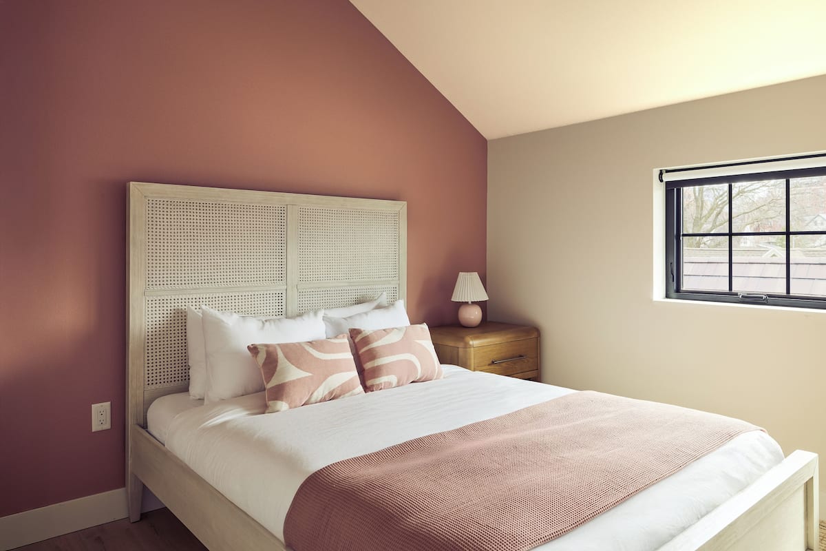 A bedroom with a bed, a nightstand, a lamp, and a window.