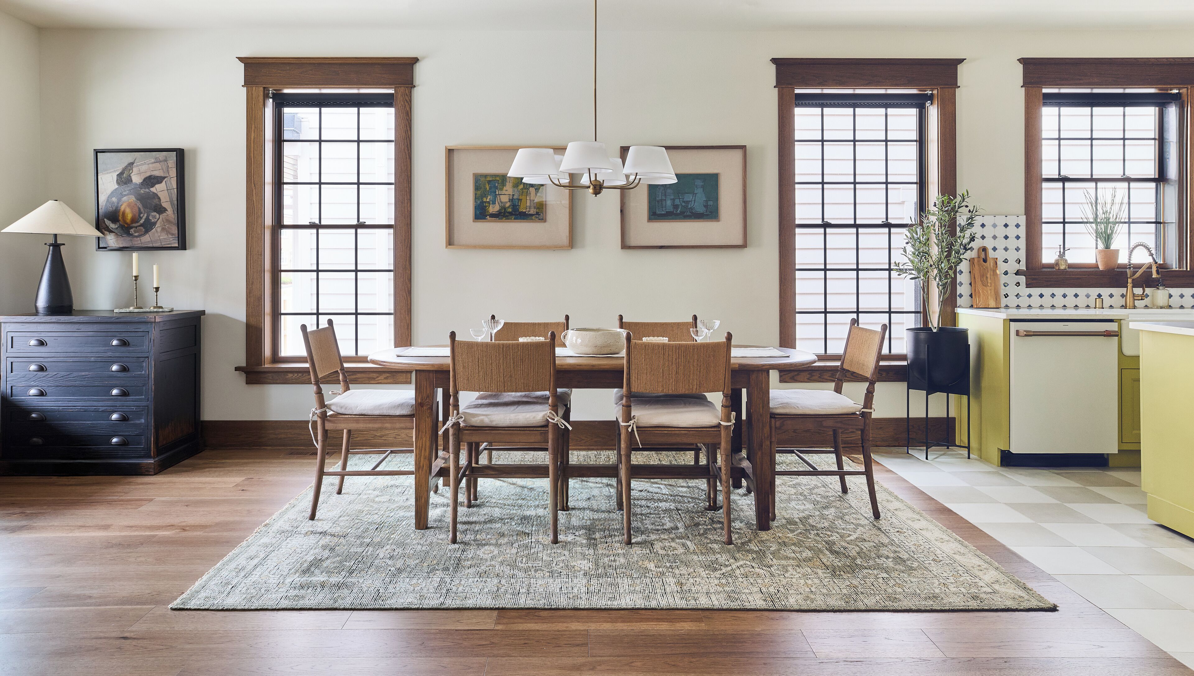 Un comedor con una mesa de madera, sillas, una araña y obras de arte en las paredes.