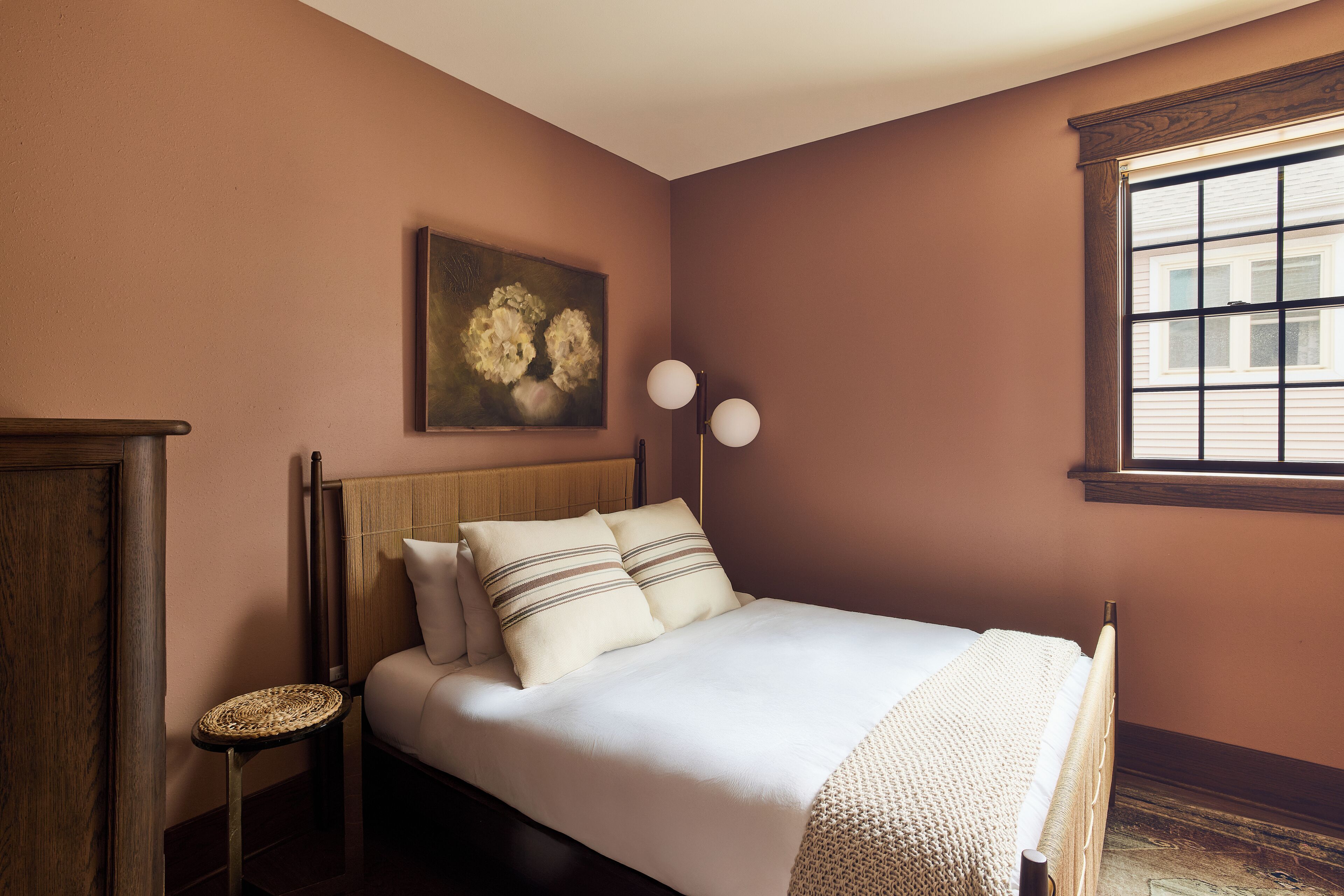 Ein Schlafzimmer mit Bett, Nachttisch, Lampe, einem Gemälde und einem Fenster.