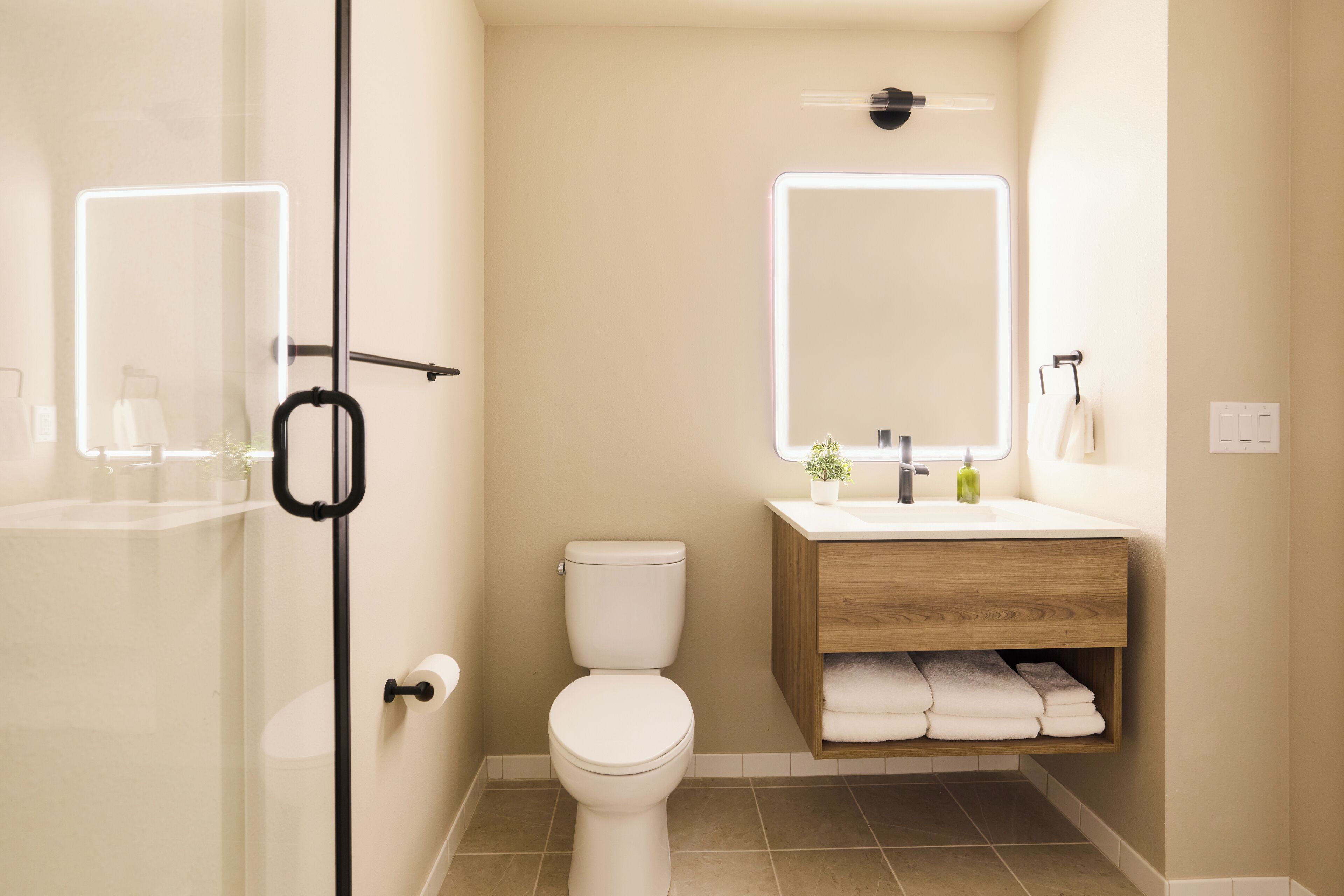 A modern bathroom with a glass shower enclosure, a toilet, a wooden vanity with a mirror, and a sink.
