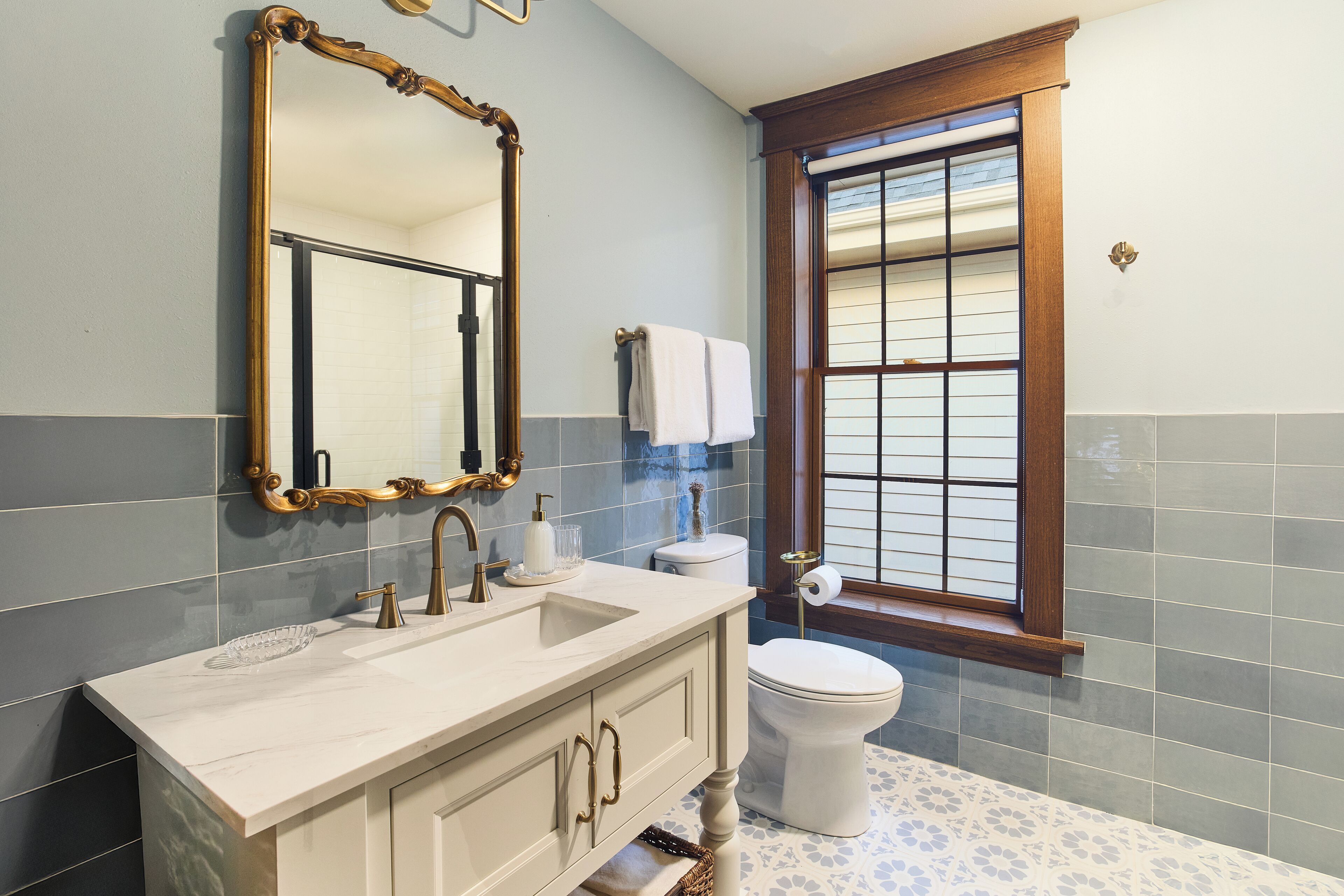 A bathroom with a vanity, sink, mirror, toilet, and window.
