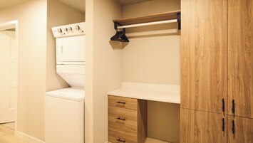 A laundry room with a white washer and dryer, wooden cabinets, and a metal shelf.