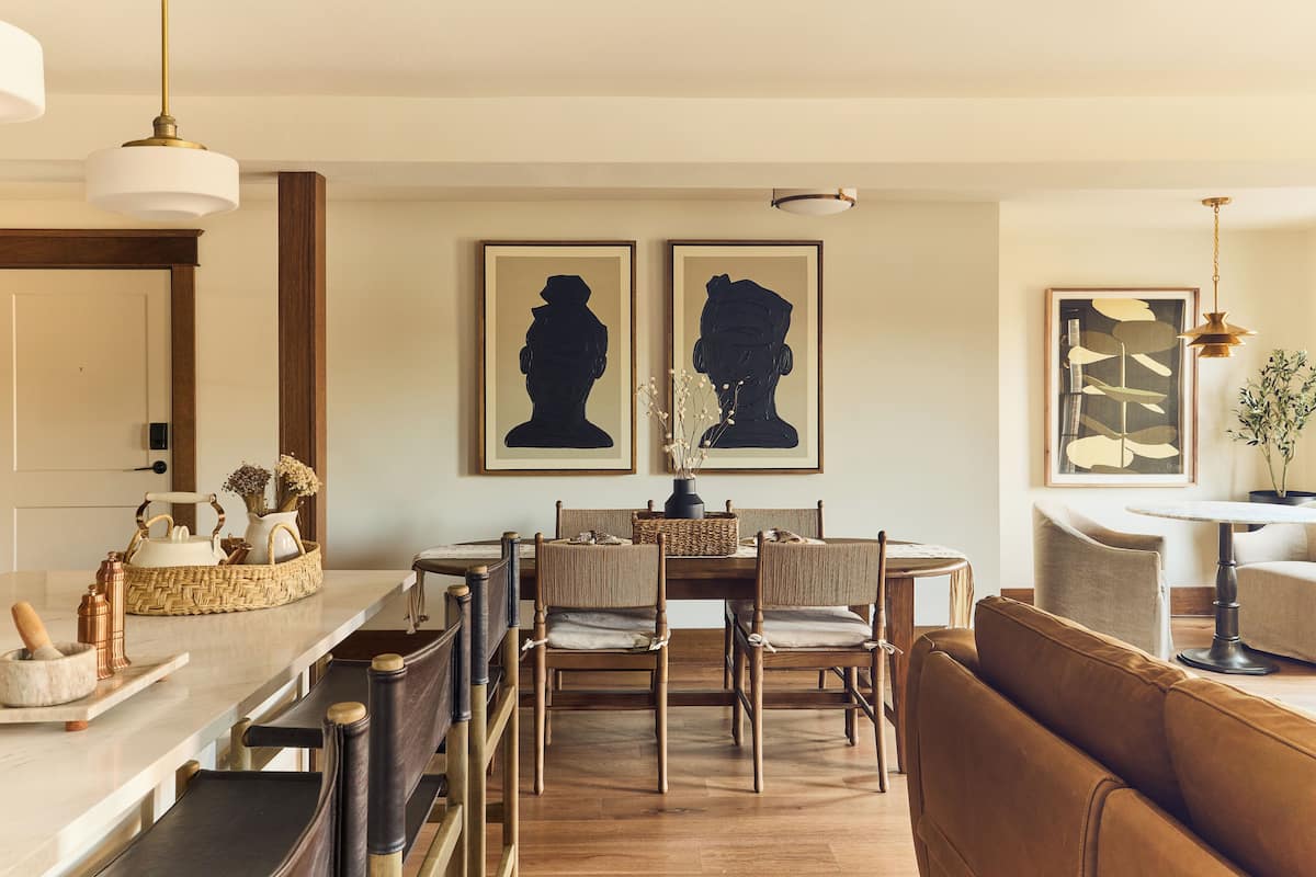 A dining area with a wooden table and chairs, a sofa, and framed artwork on the wall.