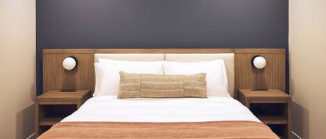 A neatly made bed with white and brown bedding, two bedside tables with lamps, and a dark wall behind the bed.