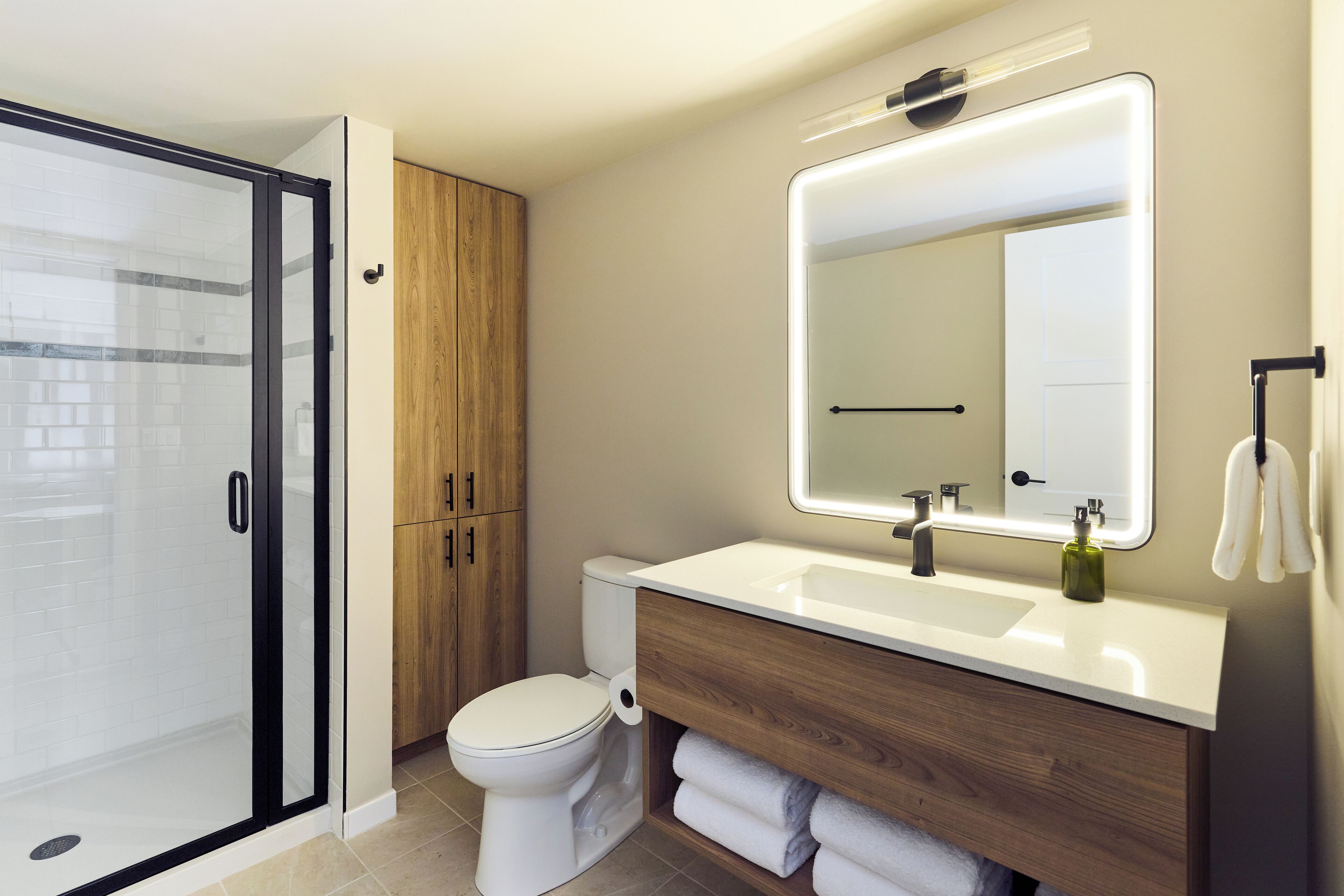 Un baño moderno con cabina de ducha de vidrio, inodoro, tocador con espejo y perchero.