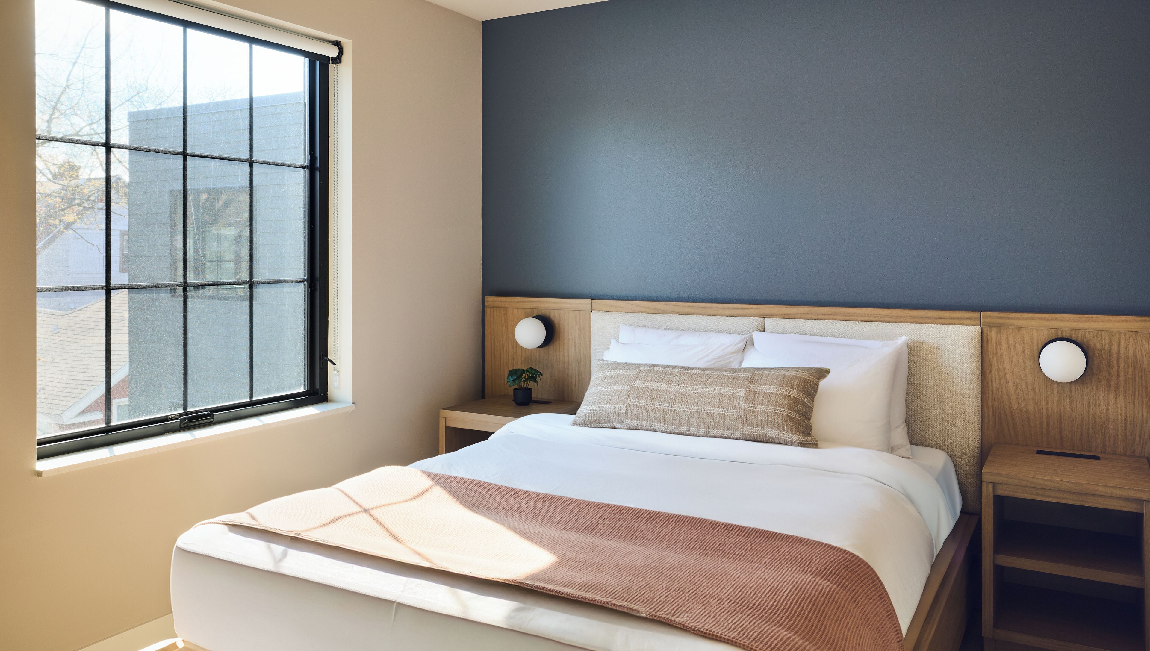 Ein Schlafzimmer mit einem Bett, Nachttischen, einem Fenster und einer Wandleuchte.