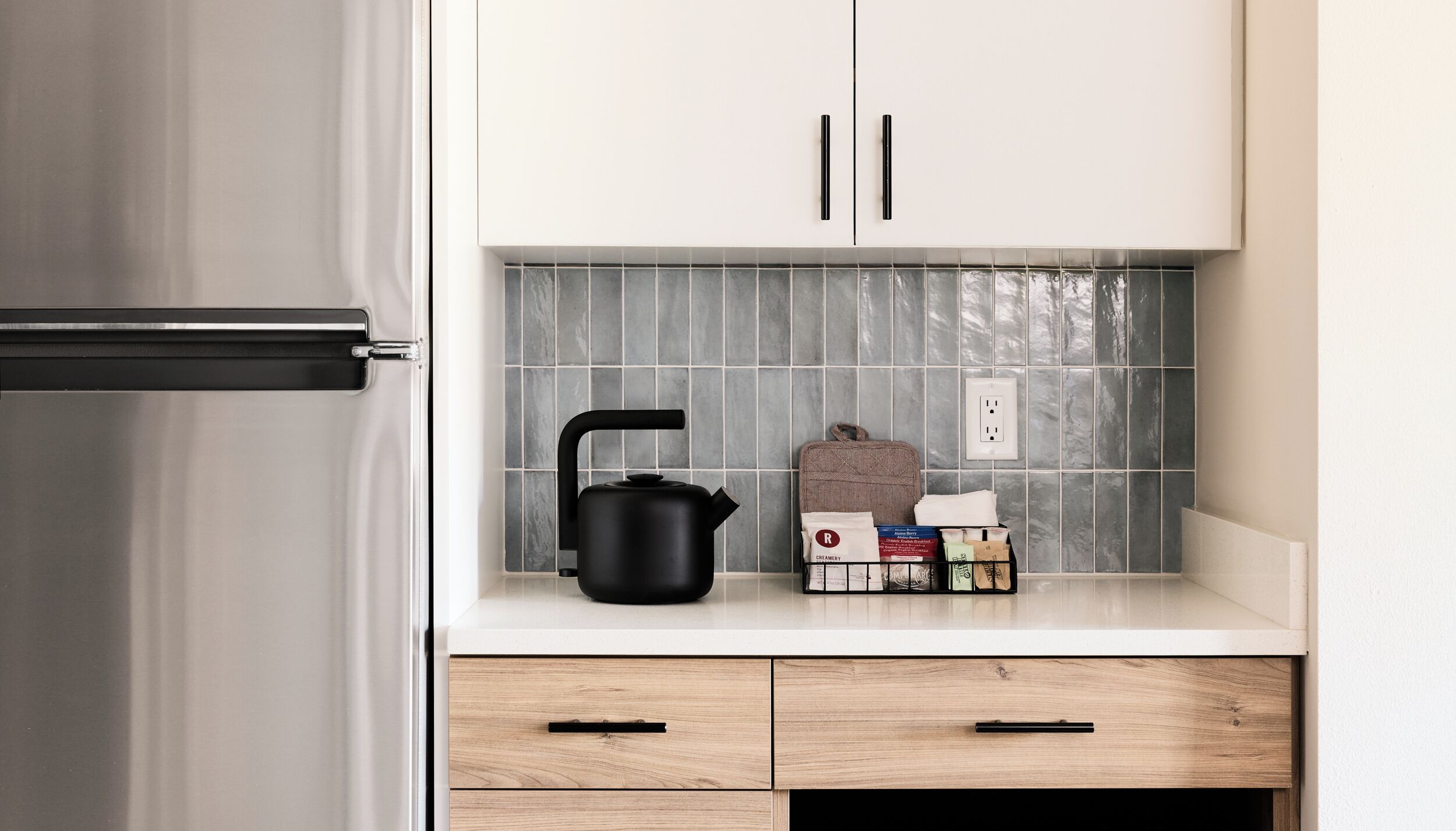 A kitchen with white cabinets, a black kettle, and a tiled backsplash.