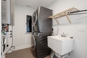 A compact laundry room with a washing machine, a drying rack, and a sink.