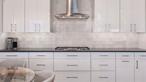 Una cocina moderna con armarios blancos, una campana de acero inoxidable y una mesa de comedor con superficie de vidrio.