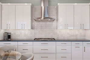 A modern kitchen with white cabinets, a stainless steel range hood, and a glass-top dining table.