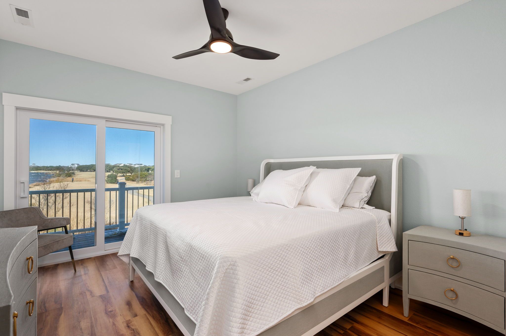 A bedroom with a bed, a nightstand, a chair, and a balcony with a view.