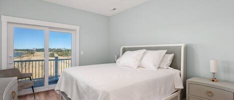 A bedroom with a bed, a nightstand, a chair, and a balcony with a view.