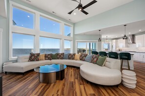 A modern living room with a curved sectional sofa, a glass coffee table, and a view of the ocean.