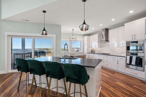 A modern kitchen with a large island, bar stools, stainless steel appliances, and a view to the outside.