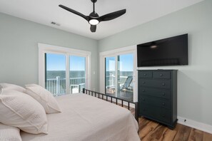 A bedroom with a bed, a dresser, a ceiling fan, and a TV. - Kite Surf Cottage: Stunning Soundfront Home, Panoramic views of the Sound and Sunset (Nags Head)
