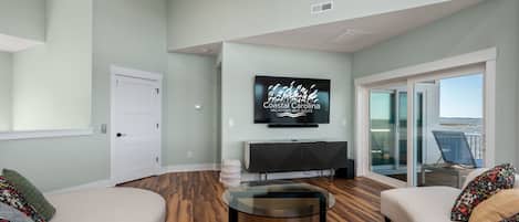 A modern living room with a flat-screen TV, a glass coffee table, and two sofas.