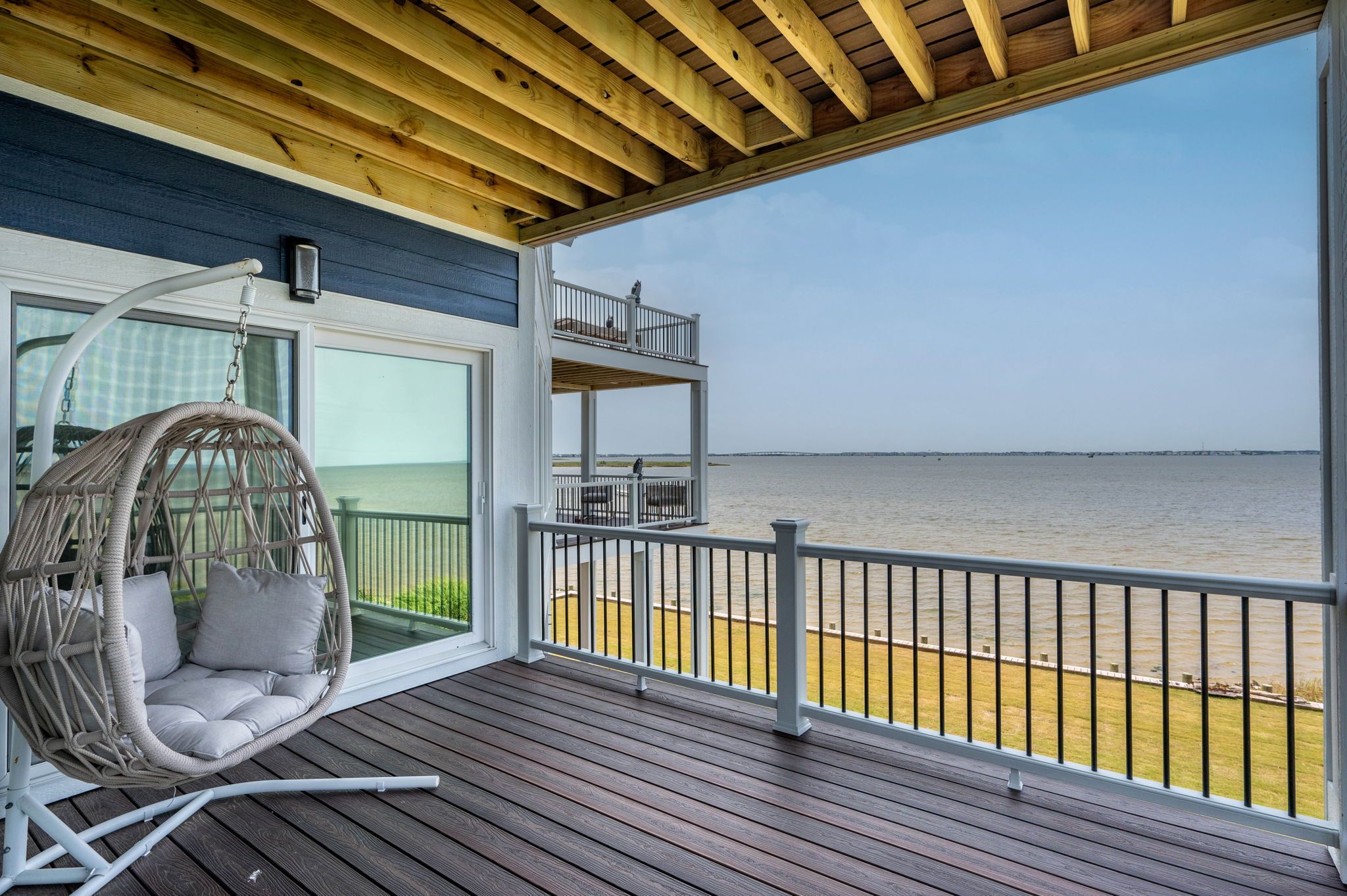 A wooden deck with a hanging chair and a balcony overlooking a body of water.