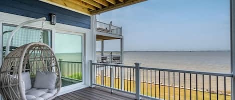 A wooden deck with a hanging chair and a balcony overlooking a body of water.