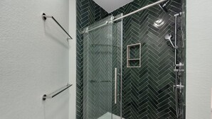 Un baño moderno con cabina de ducha de vidrio, pared de azulejos en patrón de espiga y una bañera blanca.