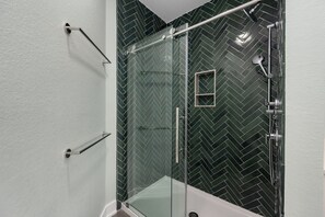 A modern bathroom with a glass shower enclosure, a herringbone-patterned tile wall, and a white bathtub.