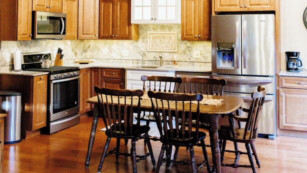 Una cocina con armarios de madera, un refrigerador de acero inoxidable, un microondas y una mesa de comedor con sillas.