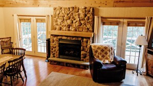 Una habitación acogedora con chimenea de piedra, muebles de madera y ventanas amplias.