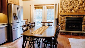 Una cocina con paneles de madera, chimenea de piedra, mesa de comedor con sillas y un refrigerador.