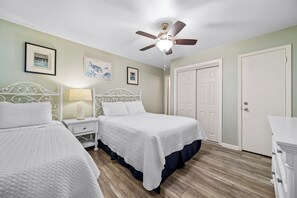 A bedroom with two beds, a ceiling fan, framed artwork, a nightstand, and a dresser. - Experience beachfront luxury at Phoenix 1117 (Orange Beach)