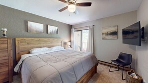 Une chambre avec un lit en bois, un ventilateur de plafond, une télévision et des œuvres d’art accrochées aux murs.