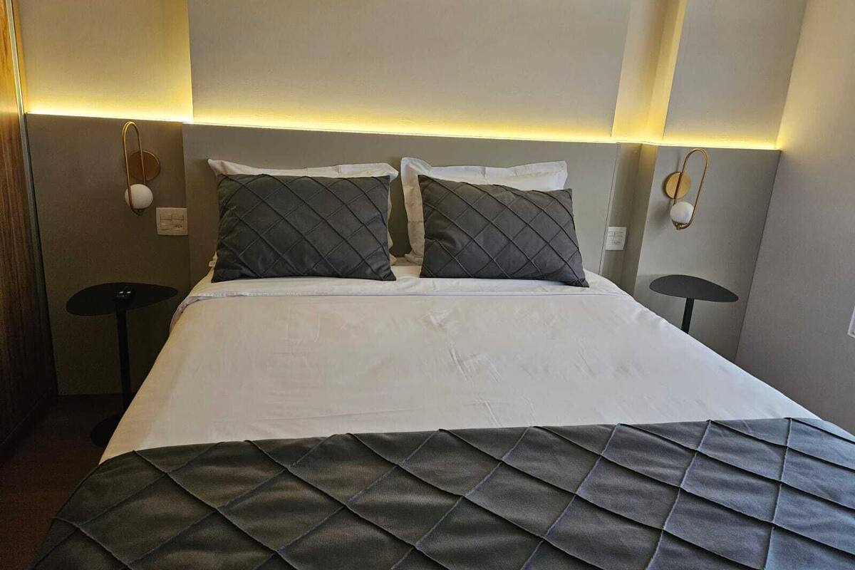 Une chambre d’hôtel avec un lit, deux tables de chevet et des lampes fixées au mur.
