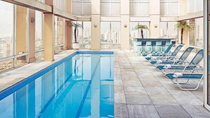 Una piscina con acqua cristallina, circondata da sdraio e ampie finestre che offrono vista sulla città.