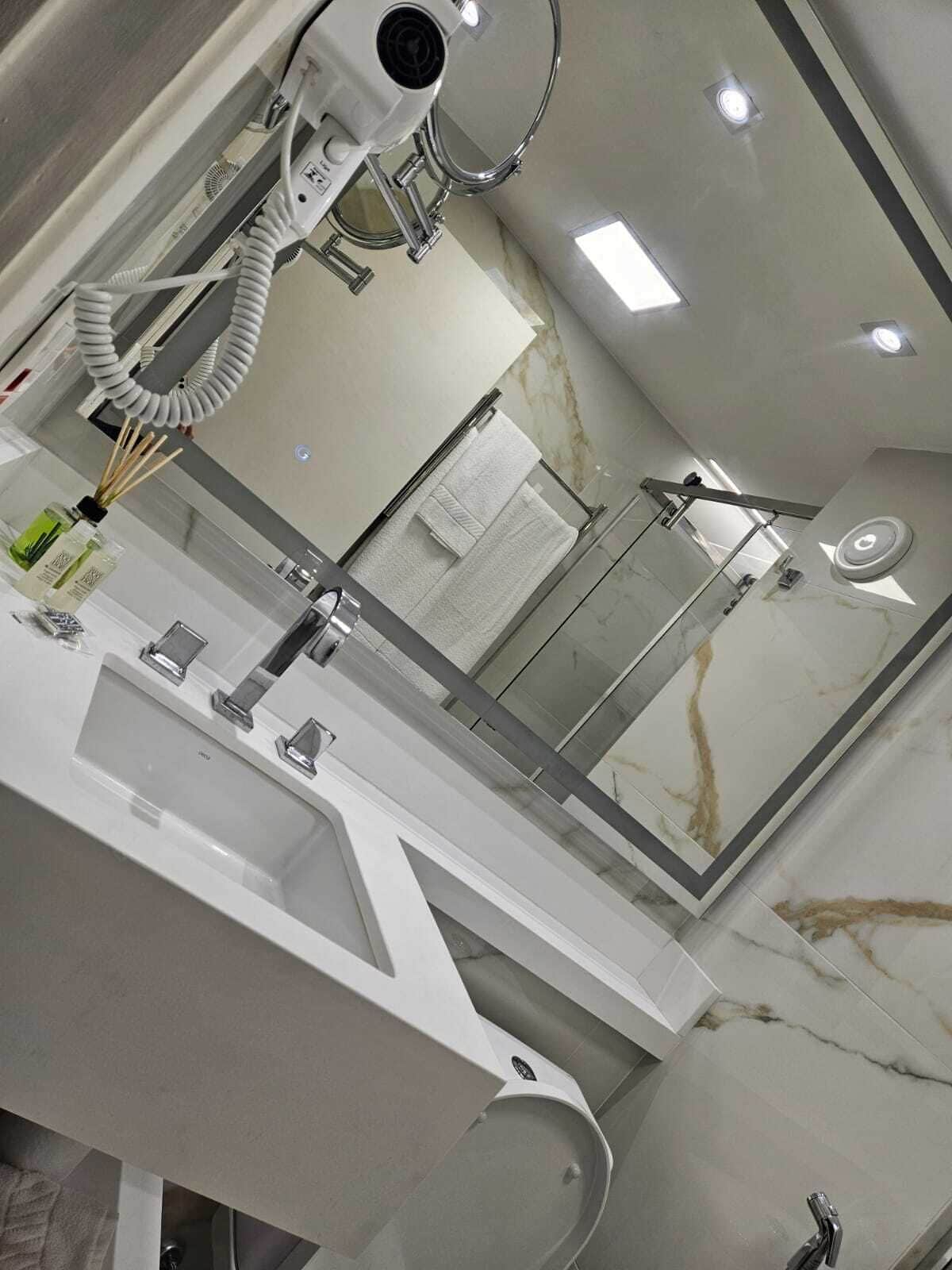 A modern bathroom with a large mirror, a sink, a toilet, and a hairdryer.