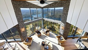 A high-ceilinged room with a large panoramic window, stone wall, and a ceiling fan. - The SkyHaüs @ Lake Burton - incredible views, hot tub, 3 grills, & porches. (Tiger)