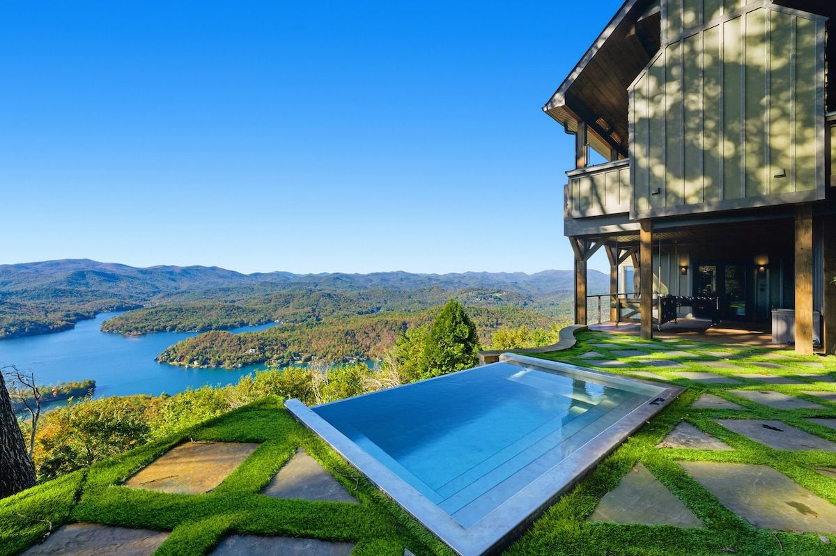 Une maison moderne dotée d’une piscine, d’un balcon et offrant une vue sur un lac et des montagnes.
