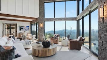 Ein geräumiges Wohnzimmer mit großem Fenster, einem runden Holztisch und Blick auf die Berge.